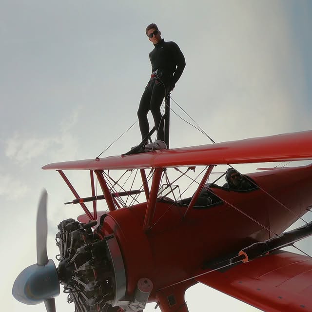Justin standing on the wing of a biplane in flight